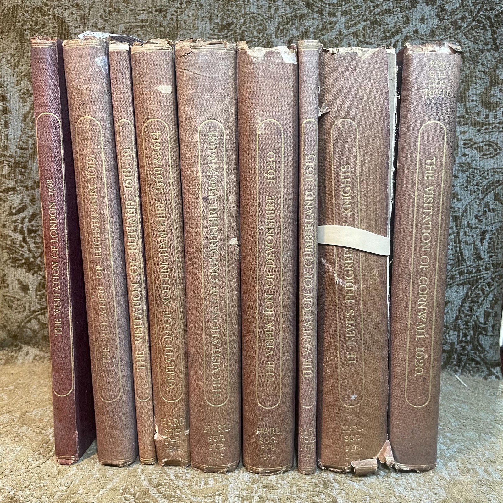 The Publications of The Harleian Society. Established A.D. 1869. Nine volumes comprising Vol.I.:The Visitation of London in the Year 1568. Taken by Robert Cooke…And Since Augmented Both With Descents and Arms. (London, 1869); Vol.II.: The Visitation of The Conty of Leicester In The Year 1619. Taken by William Camden.., Edited by John Fetherston. (London, 1870); Vol.III.:The Visitation of the County of Rutland In the Year 1618-19. Taken by William Camden... And Other Descents of Families Not in the Visitation. (London, 1870); Vol. IV.: The Visitations of The County of Nottingham In The Years 1569 and 1614, With Many other Descents of the Same County. Edited by George William Marshall, LL.M. (London, 1871); Vol. V.: The Visitations of The County of Oxford Taken in The Years 1566 by William Harvey, Clarencieux; 1574 by Richard Lee, Portcullis,.. and in 1634 by John Philpot, Somerset, and William Ryley, Bluemantle... Together with The Gatherings of Oxfordshire, Collected by Richard Lee in 1574. Edited and Annotated by William Henry Turner. (London, 1871); Vol. VI.: The Visitation of The County of Devon In The Year 1620. Edited by Frederic Thomas Colby (London, 1872); Vol.VII.: The Visitation of The County of Cumberland In The Year 1615. Taken by Richard St, George... Edited by John Fetherstone, F.S.A.(London, 1872); Vol. VIII.: Le Neve's Pedigrees of The Knights made By King Charles II., King James II., King William III. and Queen Mary, King William Alone, and Queen Anne. Edited by George w. Marshall, LL.D...(LOndon, 1873); Vol. IX.: The Visitation of the County of Cornwall, In The Year 1620. Edited by Lieut.-Colonel J.L. Vivian and Henry H. Drake, M.A., Ph.D....(London, 1874). Nine volumes total. — photograph 2.